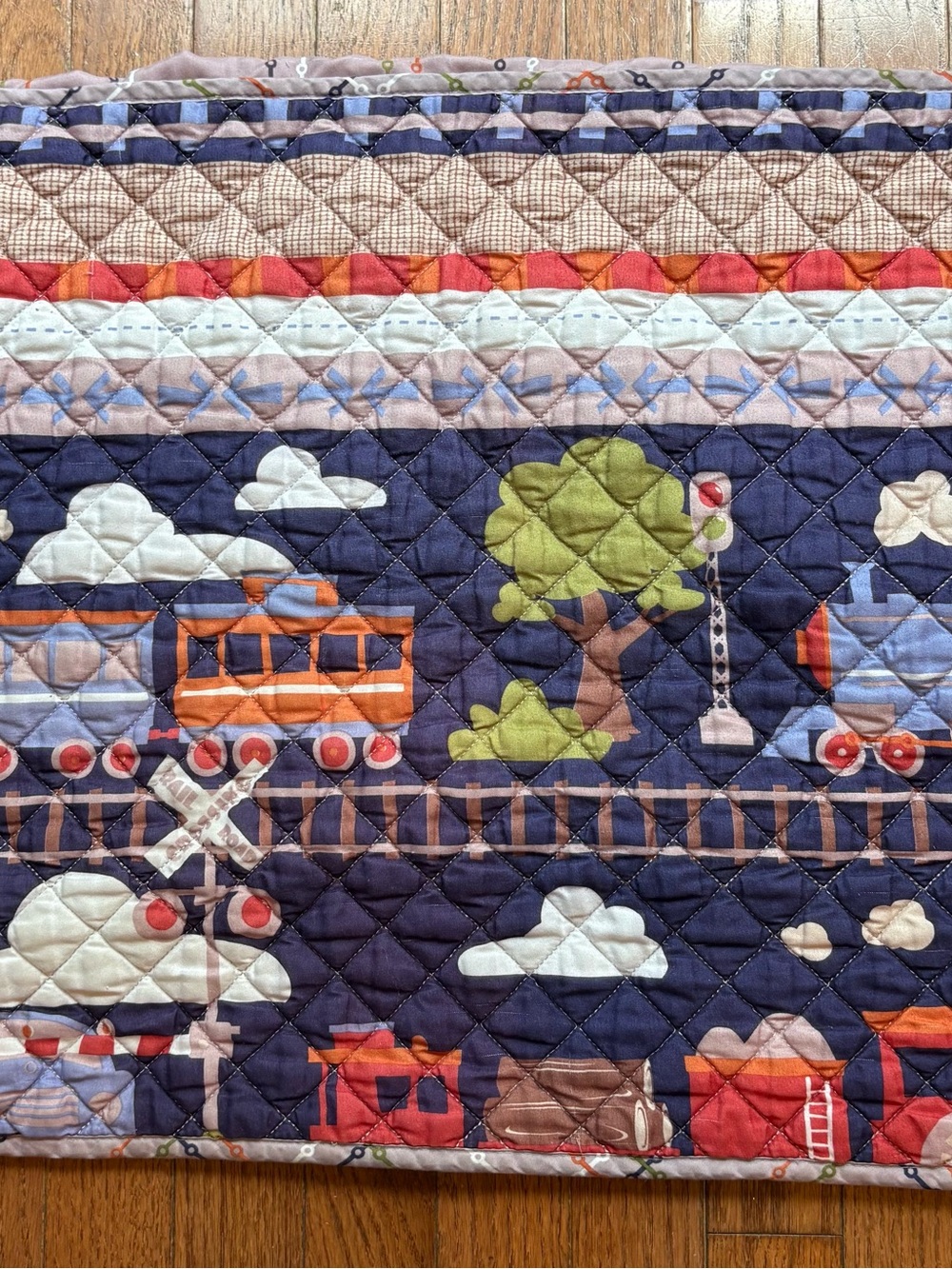 Train quilt with cartoon trains, trees, and clouds on a dark blue background.